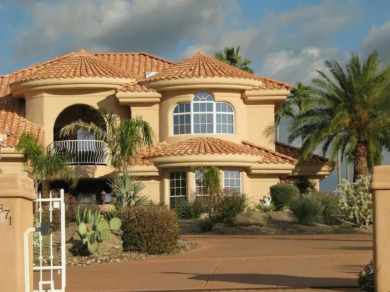 A beige stucco house with a clay tile roof, palms, and gravel landscaping in Gold Canyon, Arizona.