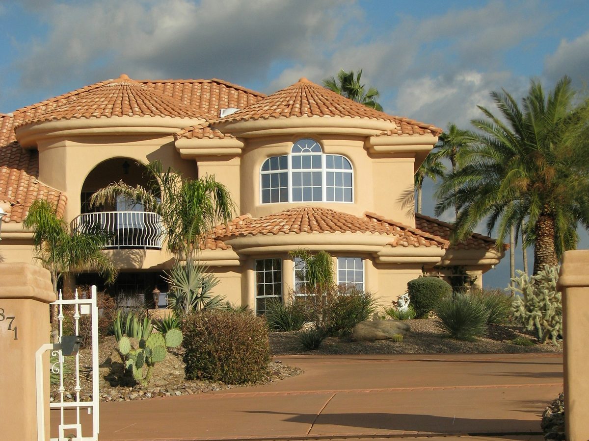 A beige stucco house with a clay tile roof, palms, and gravel landscaping in Gold Canyon, Arizona.