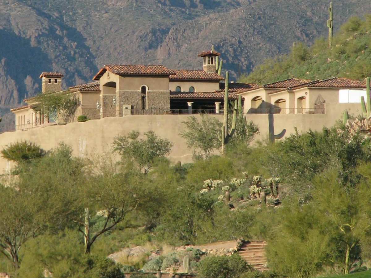 A stucco desert home with a clay tile roof and saguaros in Gold Canyon, Arizona.