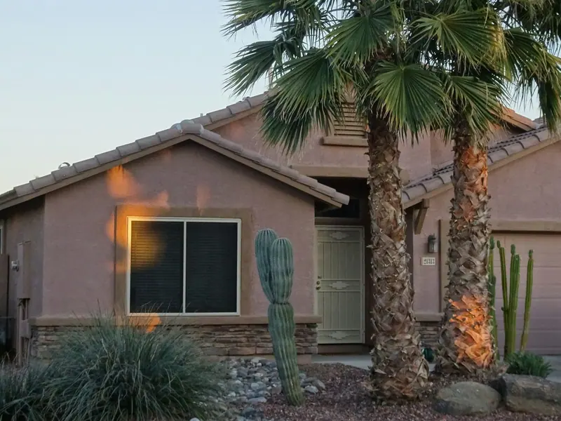 A single-story Phoenix house with a clay tile roof, gravel yard, cactus, and palm trees.