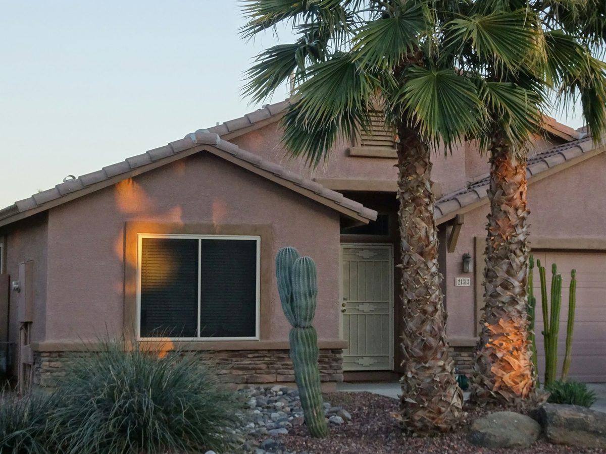A single-story Phoenix house with a clay tile roof, gravel yard, cactus, and palm trees.